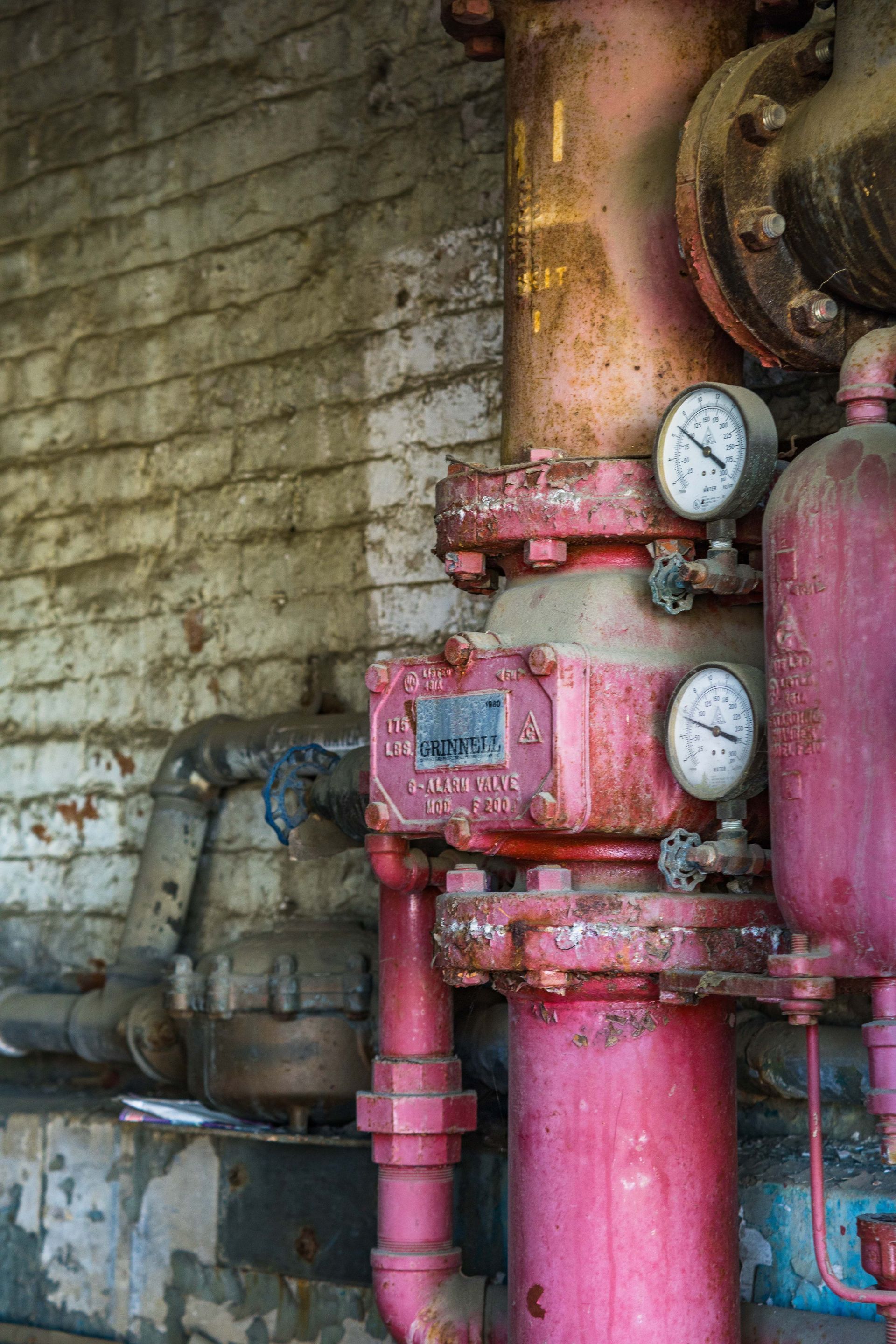 Rusty pink industrial pipes and gauges against a stained brick wall