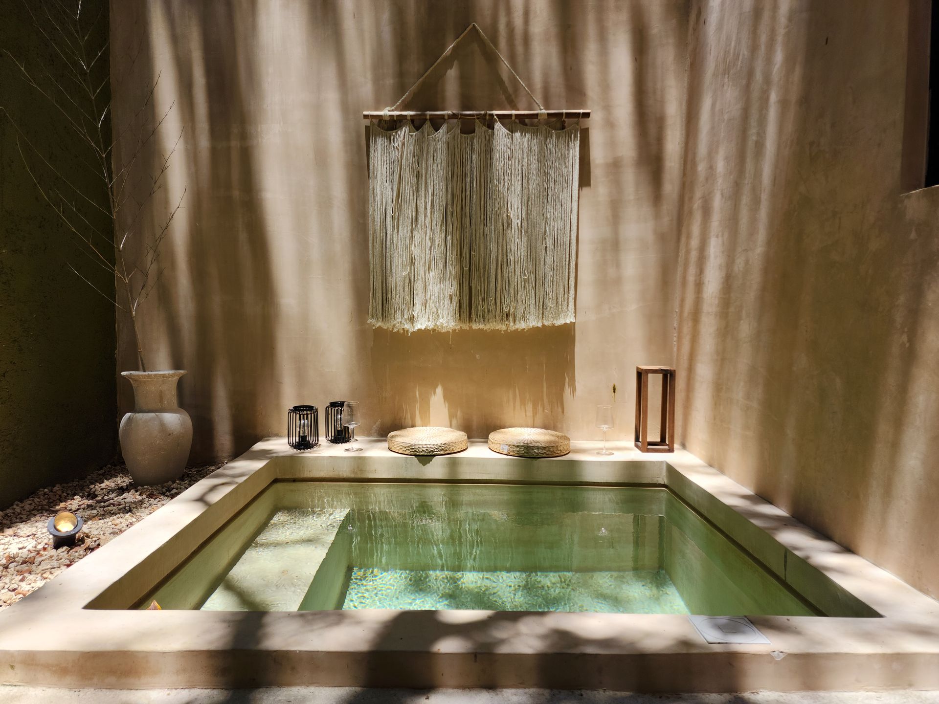Small sunlit stone courtyard with a shallow rectangular water pool and a hanging curtain waterfall