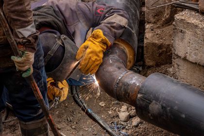 Worker welding a large metal pipe outdoors, with sparks flying in a construction trench.