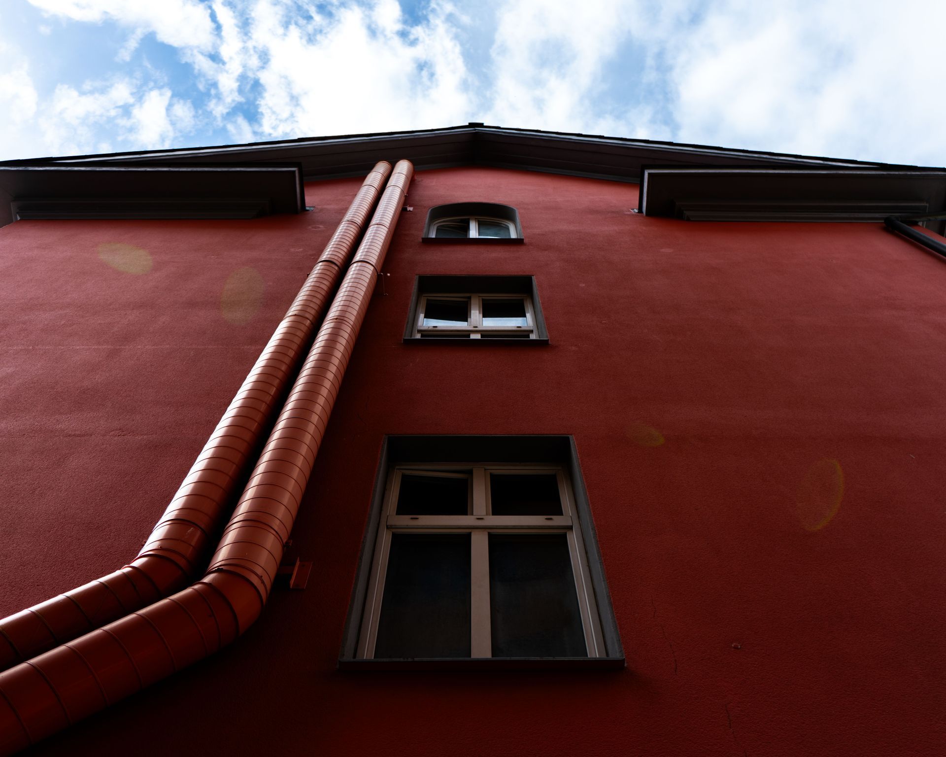 Red building facade with windows and a vertical drainpipe against the sky