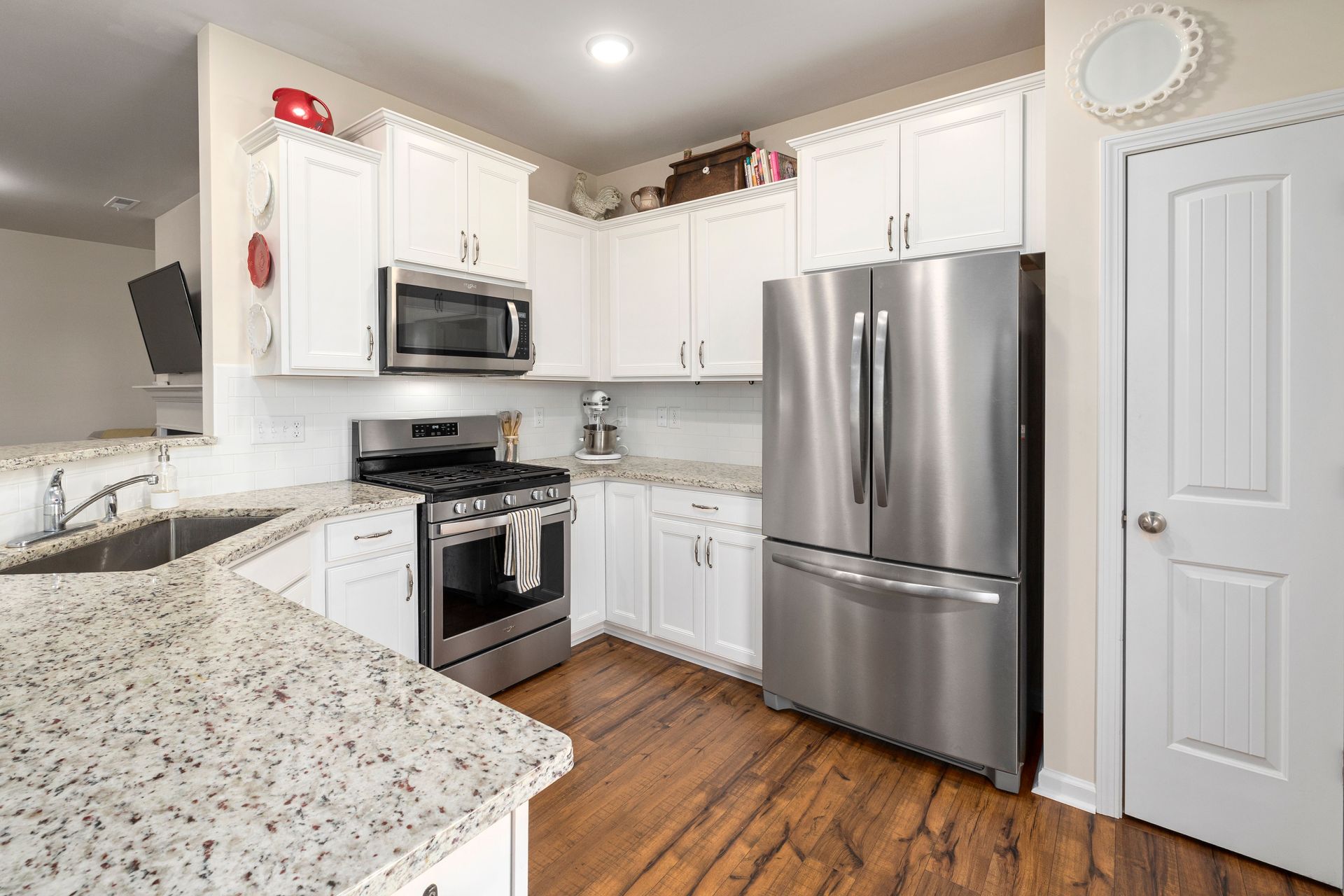 Bright white kitchen with stainless steel appliances, granite counters, and wood floors