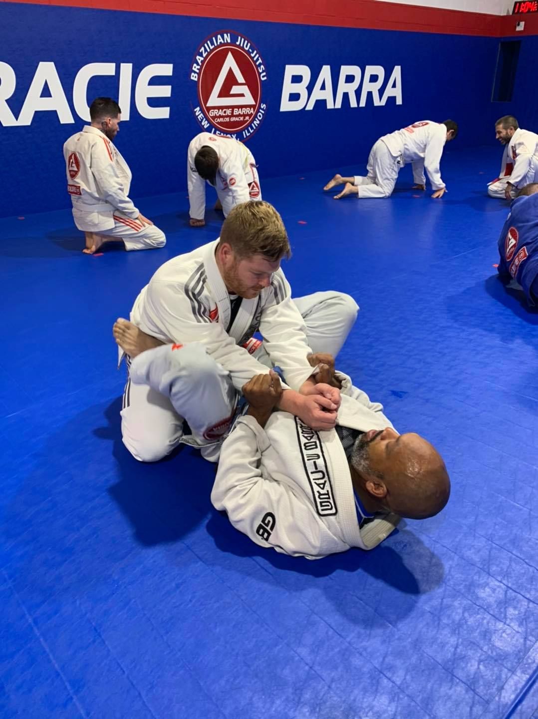 Two people practicing Brazilian Jiu-Jitsu on a mat; one in a black gi, one in a white gi, grappling.