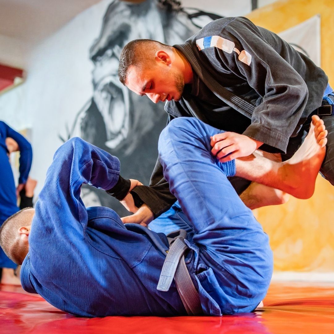 Five people in jiu-jitsu gear pose together in a gym.  Smiling,  some have arms around each other. Machado logo visible.