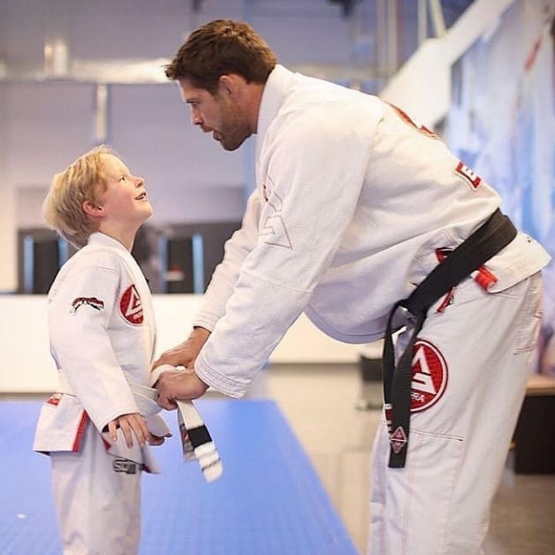 People practicing Brazilian Jiu-Jitsu. One person on the ground, another on top; two others grappling nearby. Black gis, indoor setting.