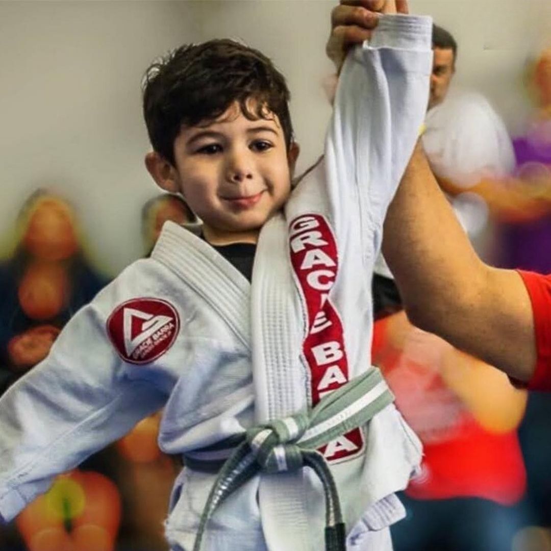 Two boys on a mat practicing Jiu-Jitsu. One boy is on top, giving a thumbs-up.