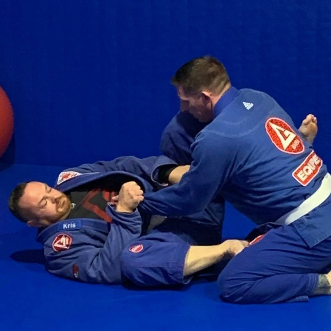 Two men grappling on a mat, one in blue, the other in black.