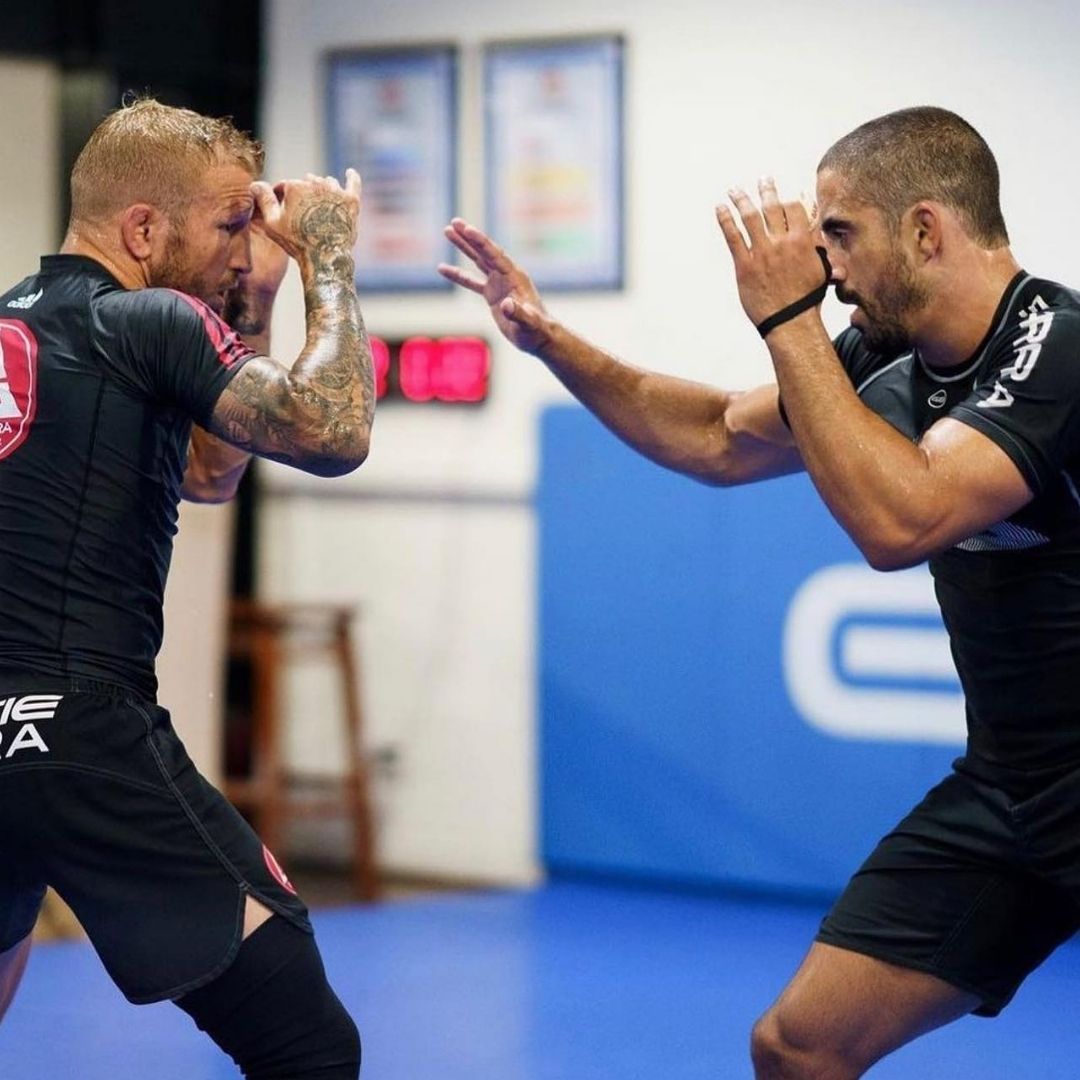Two people practicing Brazilian Jiu-Jitsu on a mat. One is on top, applying a hold.