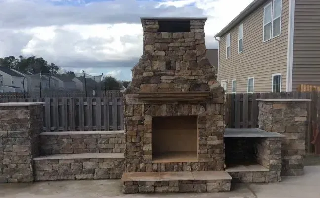 A large stone fireplace is sitting in front of a house.