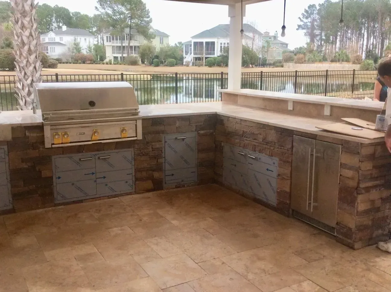 A man is standing in a kitchen with a grill and a refrigerator.