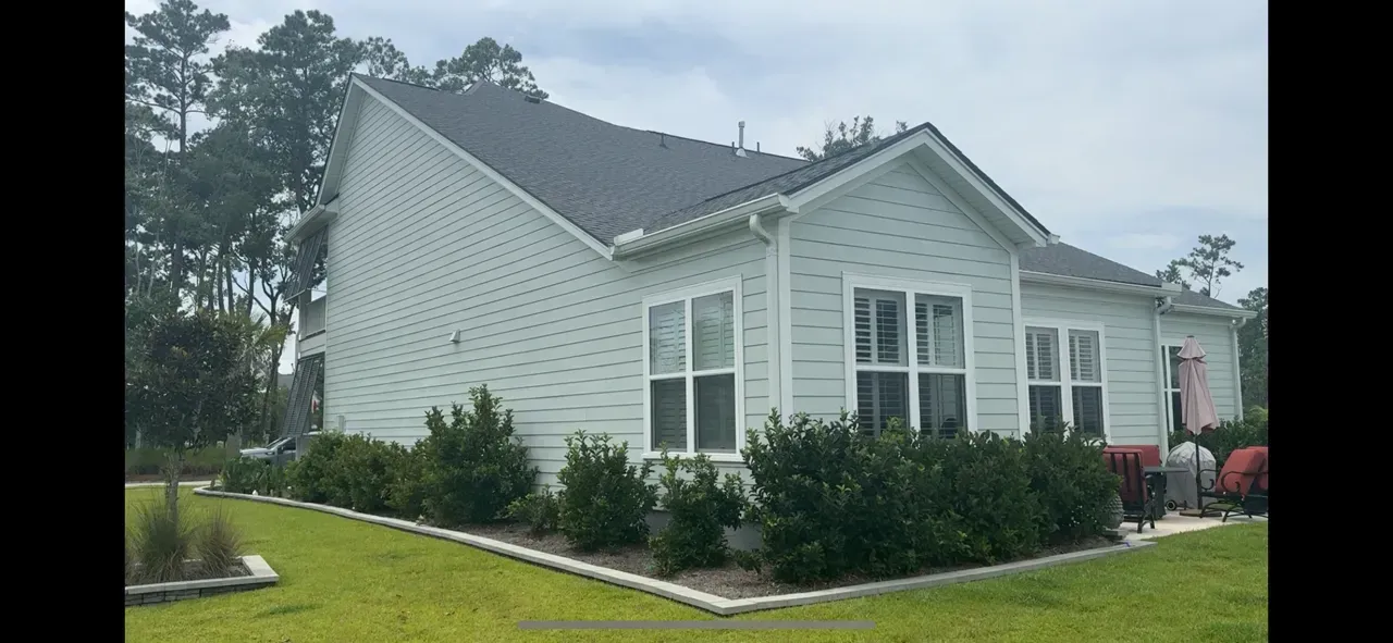 A white house with a black roof is sitting on top of a lush green lawn.