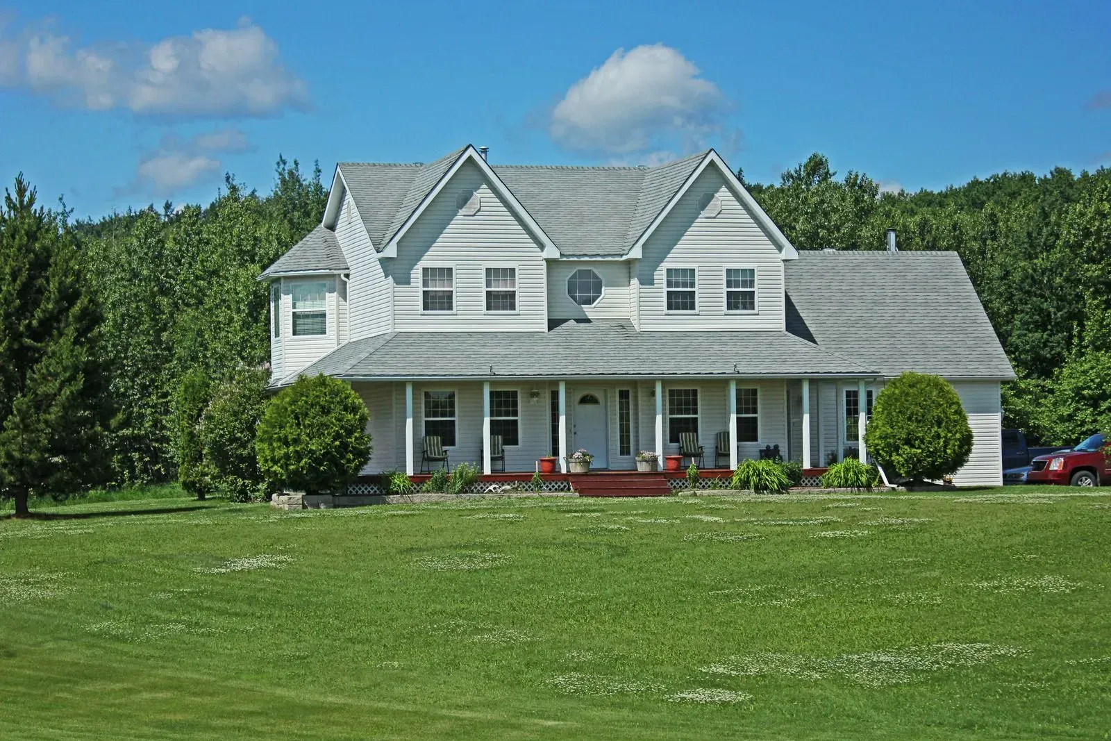 A large white house sits in the middle of a lush green field