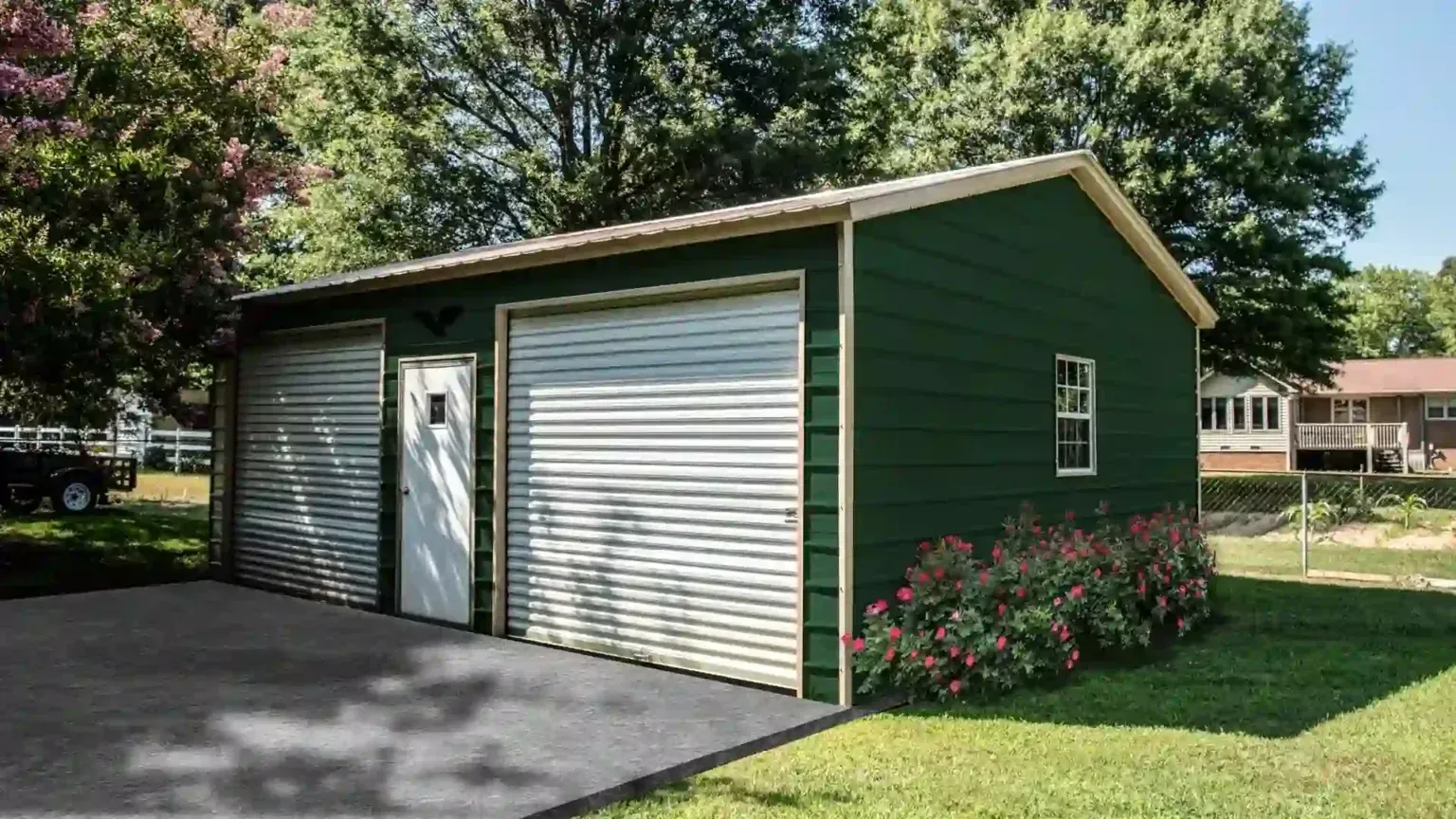 Green two-car garage with white garage doors, a white door, and small window; on a sunny day.