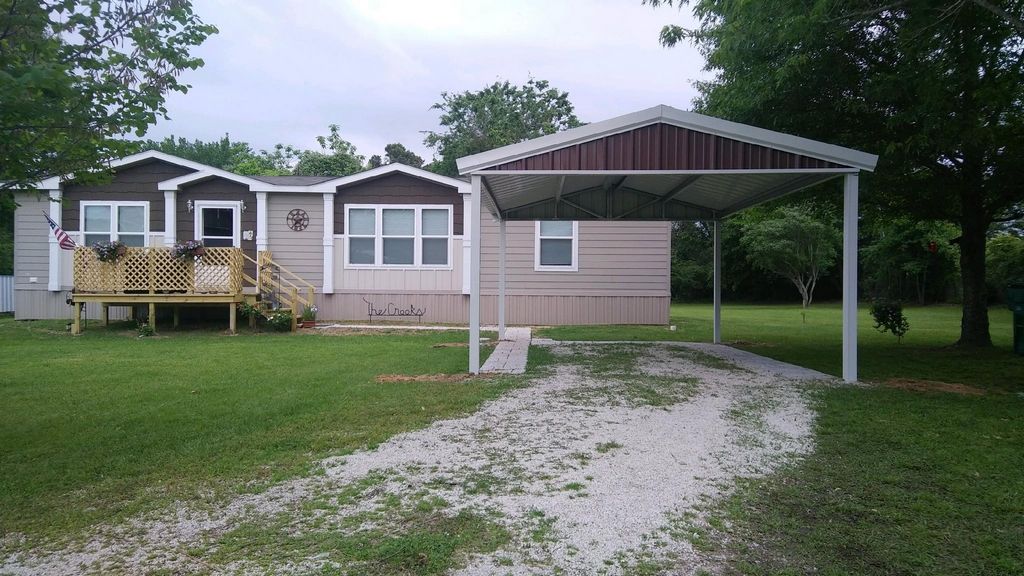 Mobile home with a brown carport and gravel driveway.