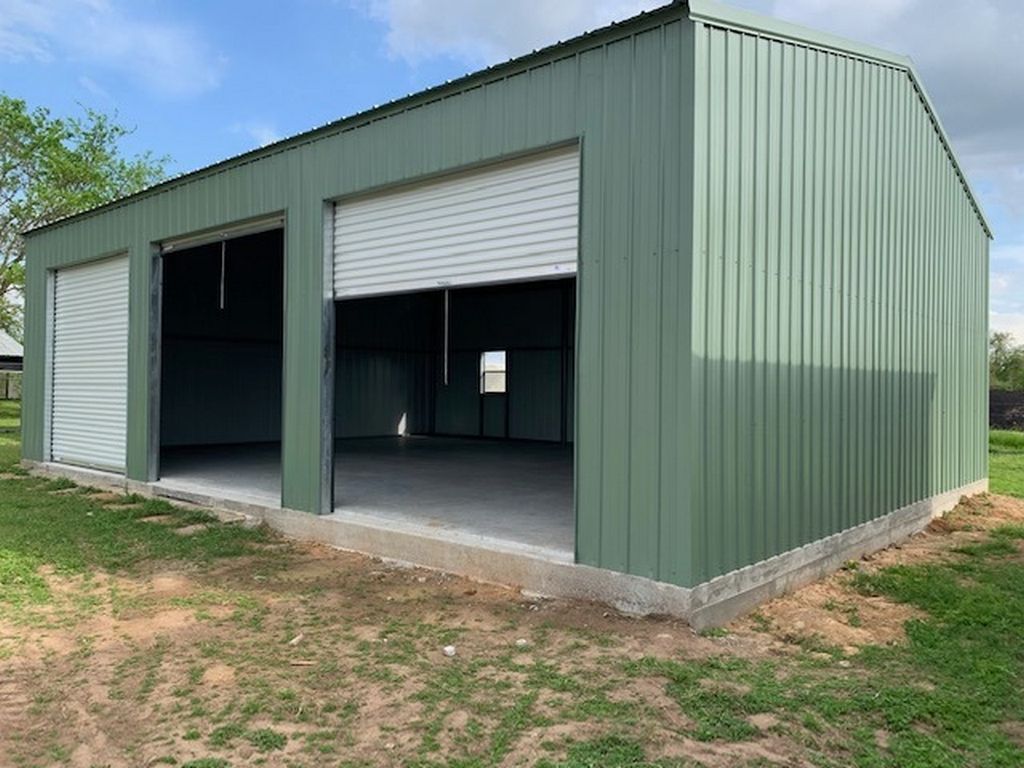 Green metal building with two open garage doors on a concrete slab, outdoors.