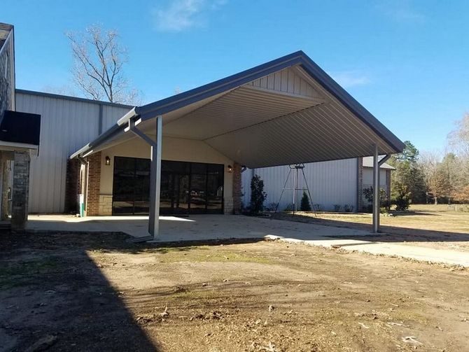 Carport in front of a building with a concrete pad and dark tinted windows. Blue sky.
