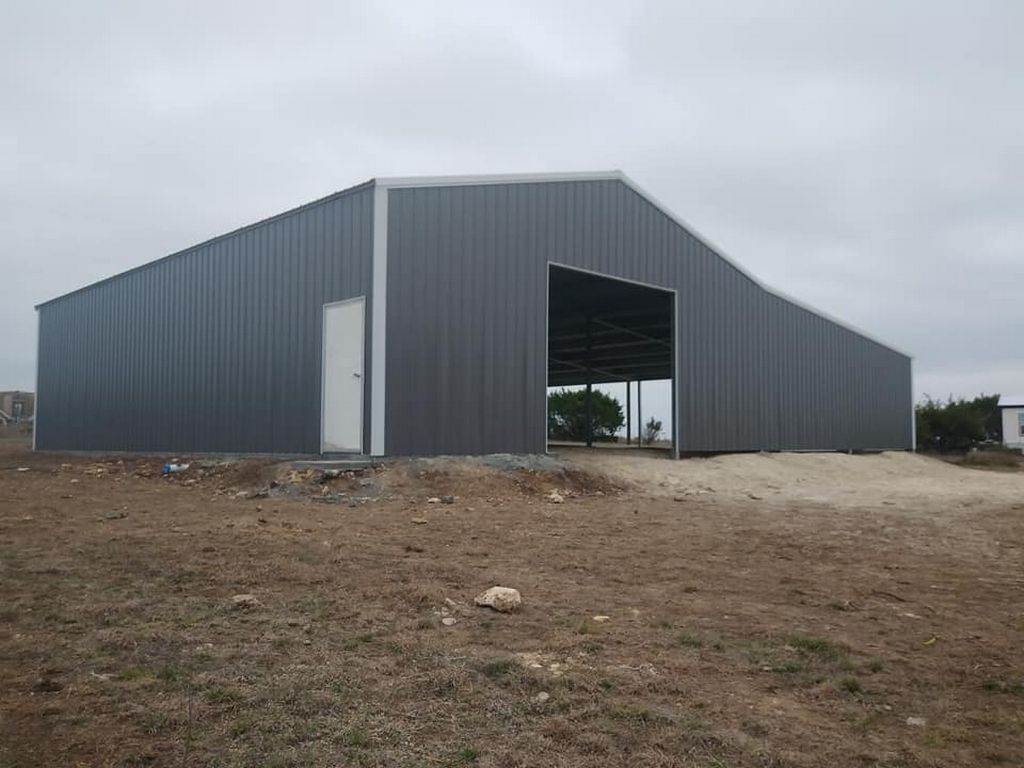 Gray metal barn with open entrance and white door, in a field under a cloudy sky.