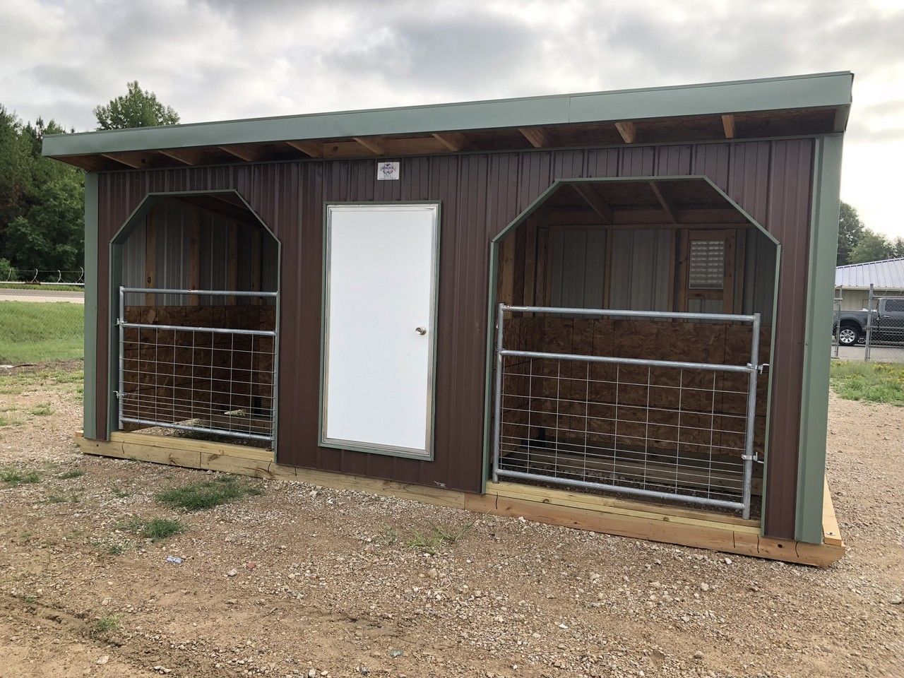Brown and tan livestock shelter with two stalls and a white door, under a cloudy sky.