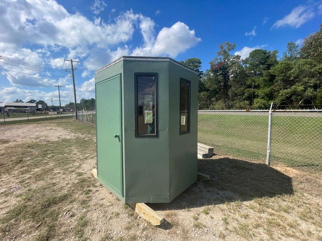 Green octagonal outdoor structure with windows and door; set in grassy area.