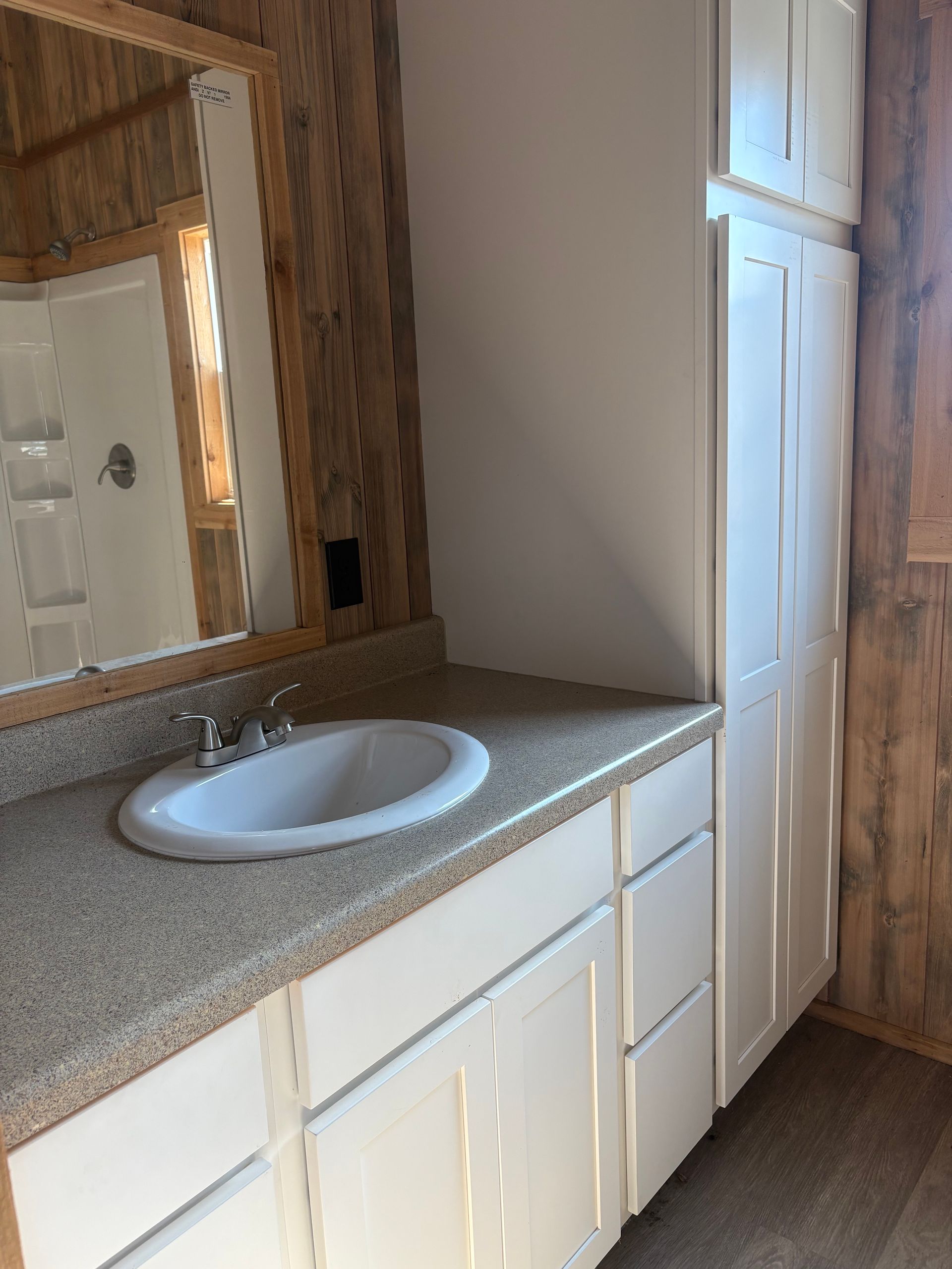 Bathroom with white cabinets, light countertop, oval sink, and wood-paneled walls.