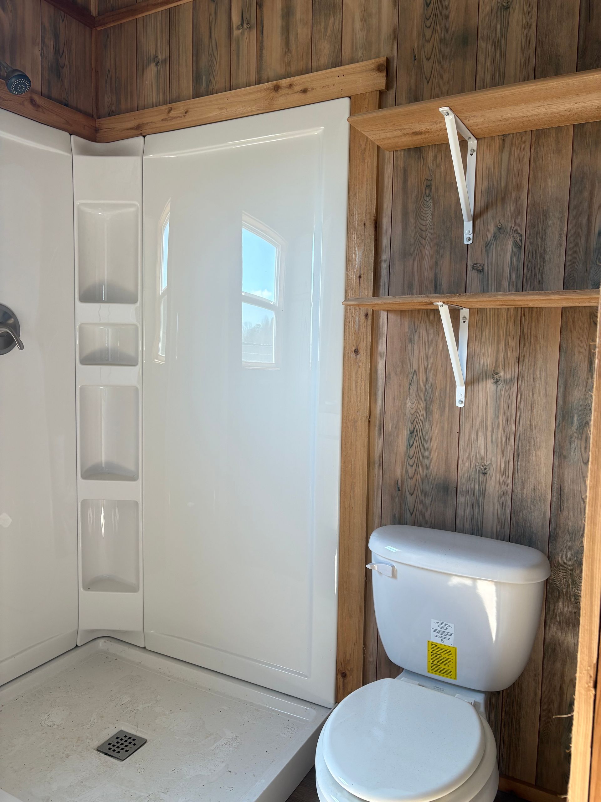 Small bathroom with a white shower, toilet, and wooden walls.