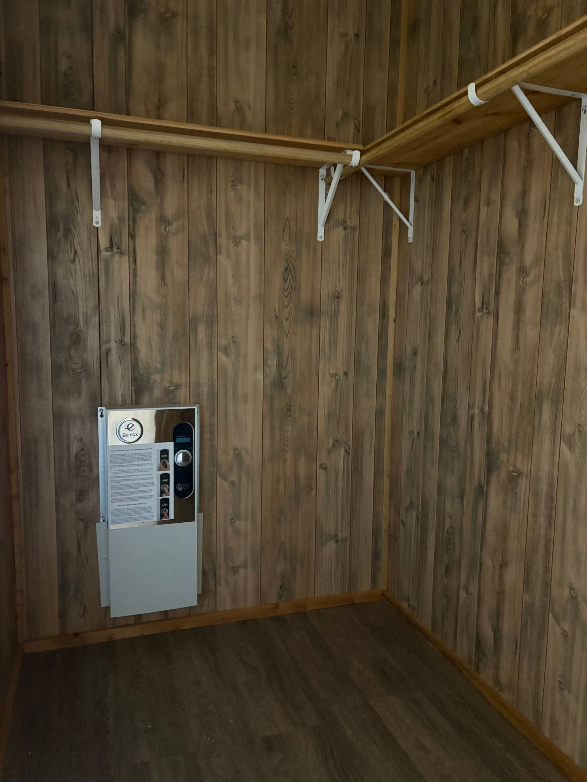 Empty wooden closet with shelves and a utility panel on the wall.