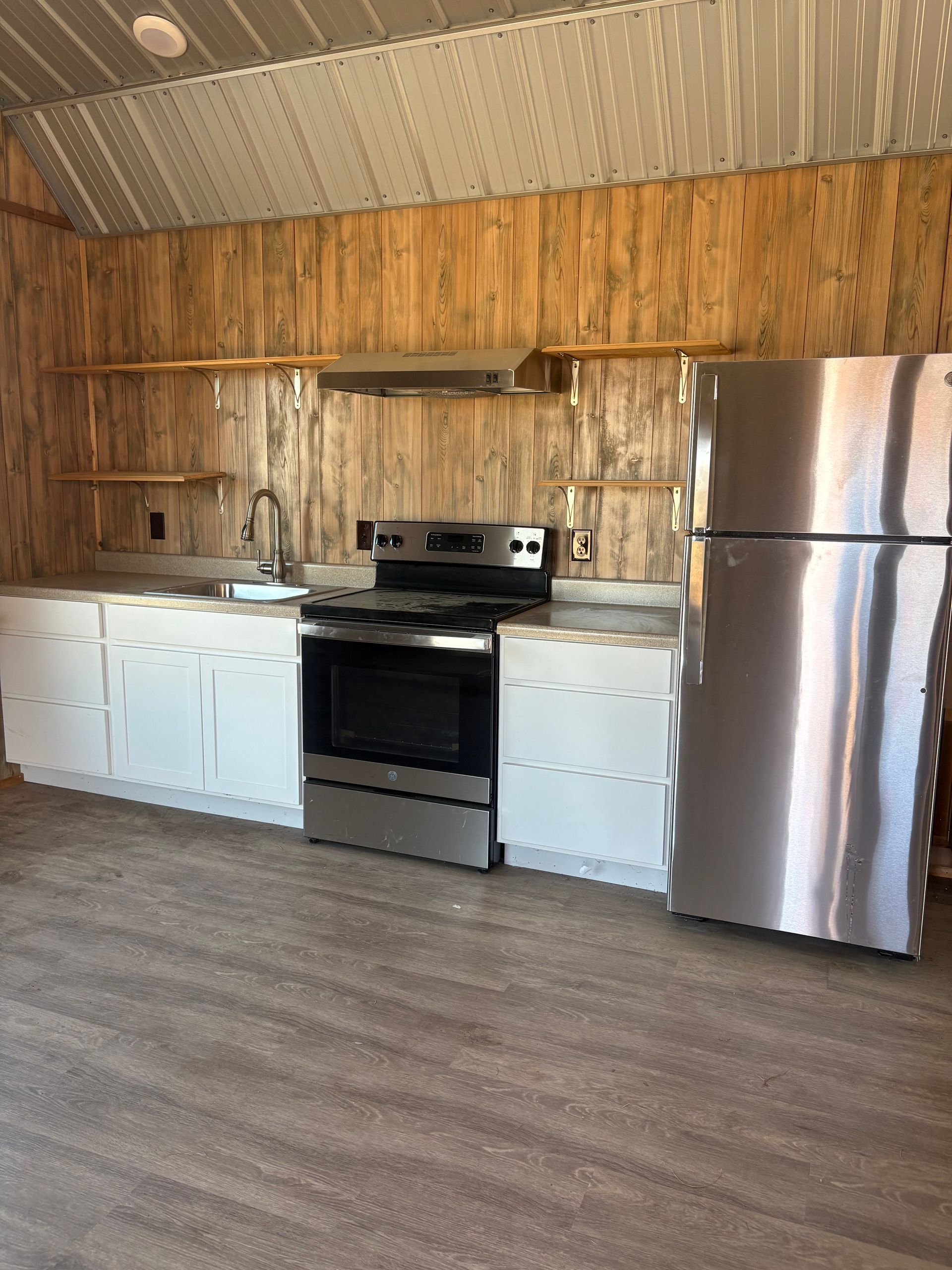 Kitchen with white cabinets, stainless steel appliances, wood paneling, and floating shelves.