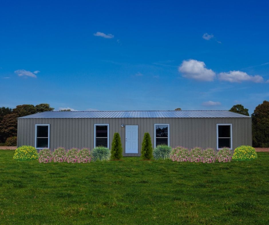 Metal building with windows, door, and landscaping, set against a blue sky with clouds, on a grassy field.