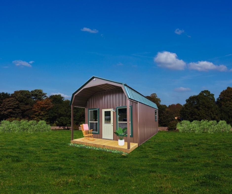 Brown metal barn-style cabin with porch, door, and windows, set in a grassy field under a blue sky.