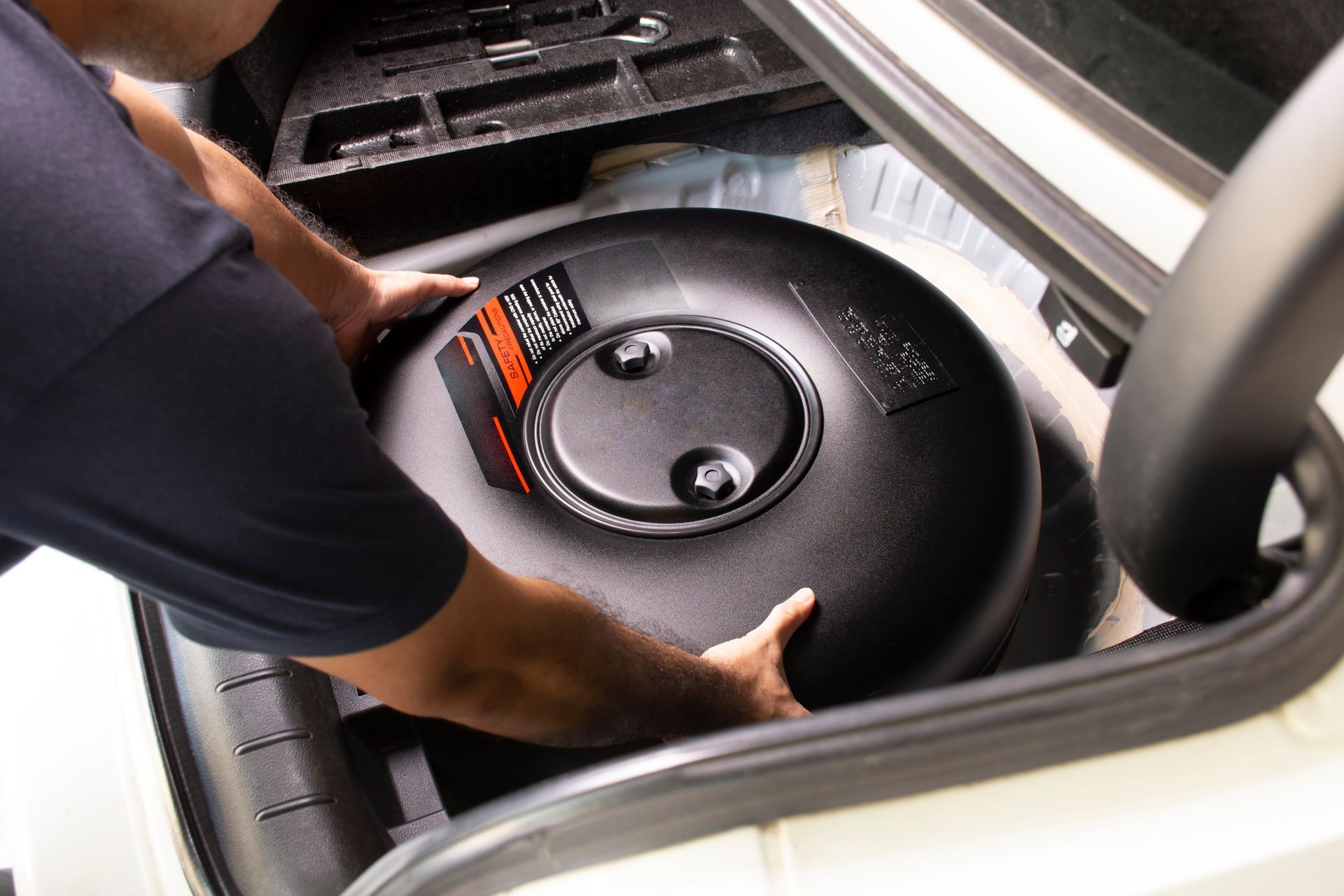 A Person Installing a Large, Black Fuel Tank in the Trunk of a Car — Warners Bay Tyre & Mechanical in Warners Bay, NSW