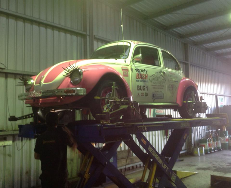 Pink and White VW Beetle on a Lift in a Garage, Being Worked on — Warners Bay Tyre & Mechanical in Warners Bay, NSW