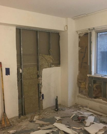 Room undergoing renovation; exposed wall studs, insulation, and debris on floor.