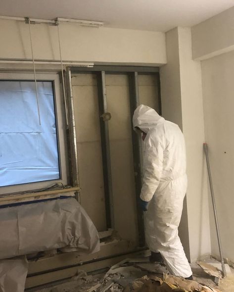 Person in protective suit working on a wall, construction setting.