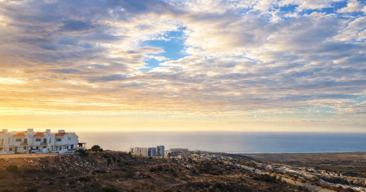 Vista costera al atardecer, edificios blancos, océano, cielo nublado con toques dorados y azules para casas en Tijuana