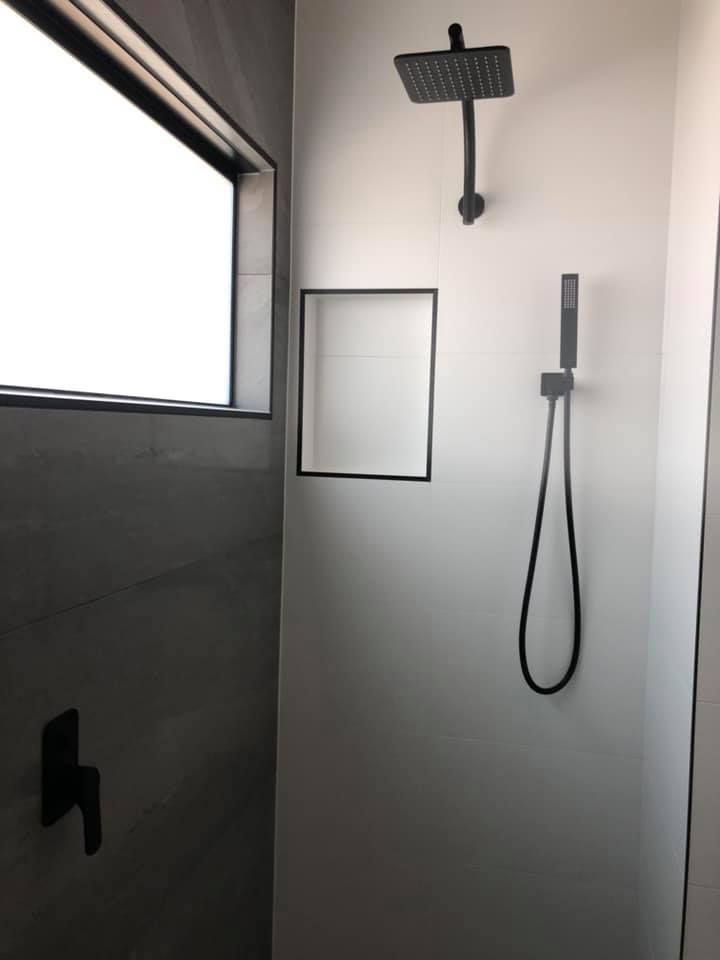 A shower with a black shower head and a window