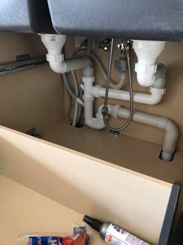 A kitchen sink with a lot of pipes underneath it.