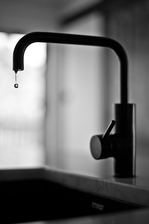 A black and white photo of a kitchen sink with a drop of water coming out of the faucet.