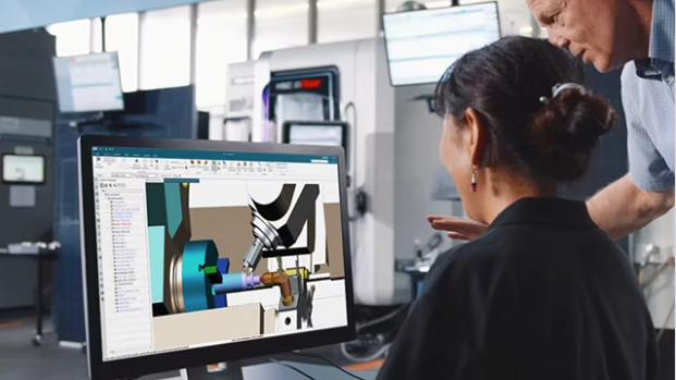 Woman and man review 3D model on computer in a manufacturing environment, machine tools in background.