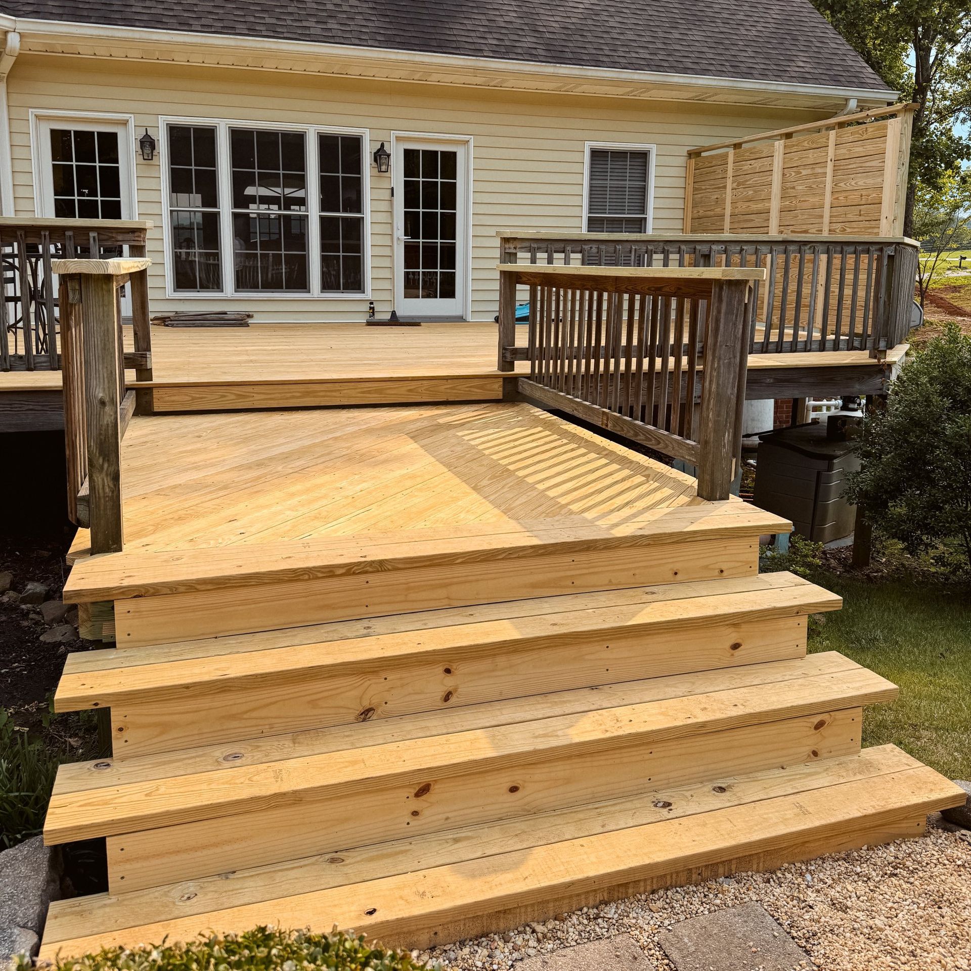 Wooden deck with steps leading down, attached to a light-colored house.