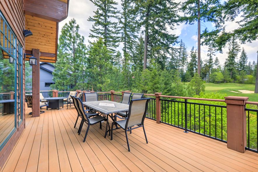 A wooden deck with a dining table and chairs, overlooking a golf course. Surrounded by trees.