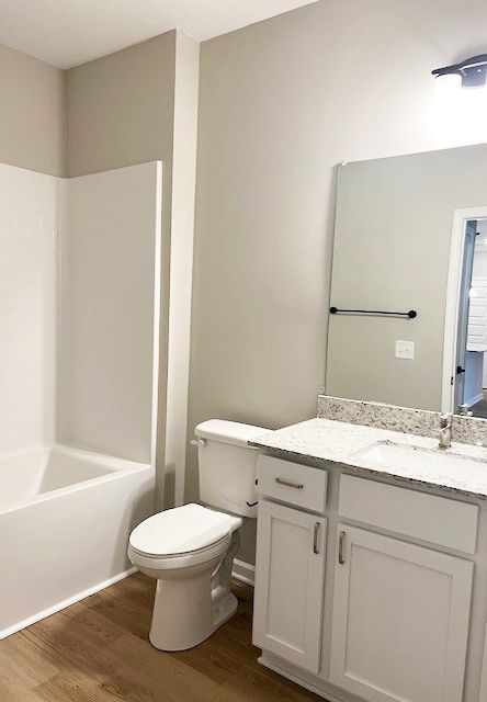 Bathroom with white tub, toilet, vanity, and light-colored walls. Wood-look flooring.
