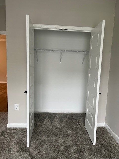 Closet with white bi-fold doors, open. The interior has a wire shelf and clothes rod. Grey carpet.
