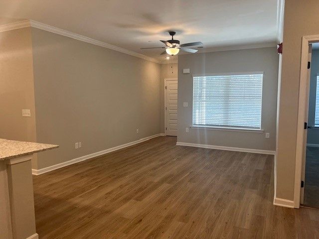 Empty living room with light brown wood-look flooring, beige walls, and a ceiling fan.