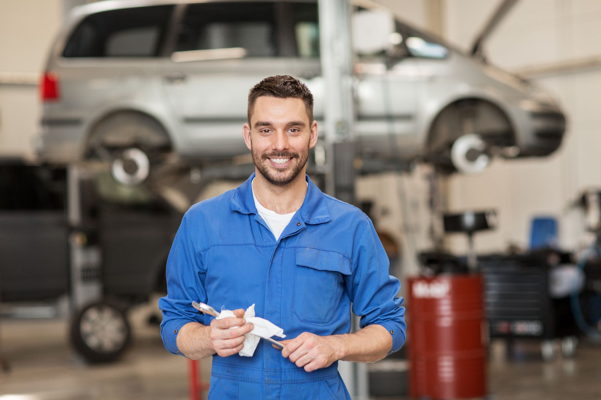 A smiling auto mechanic looking at the camera with a spanner in his hand at a car workshop.