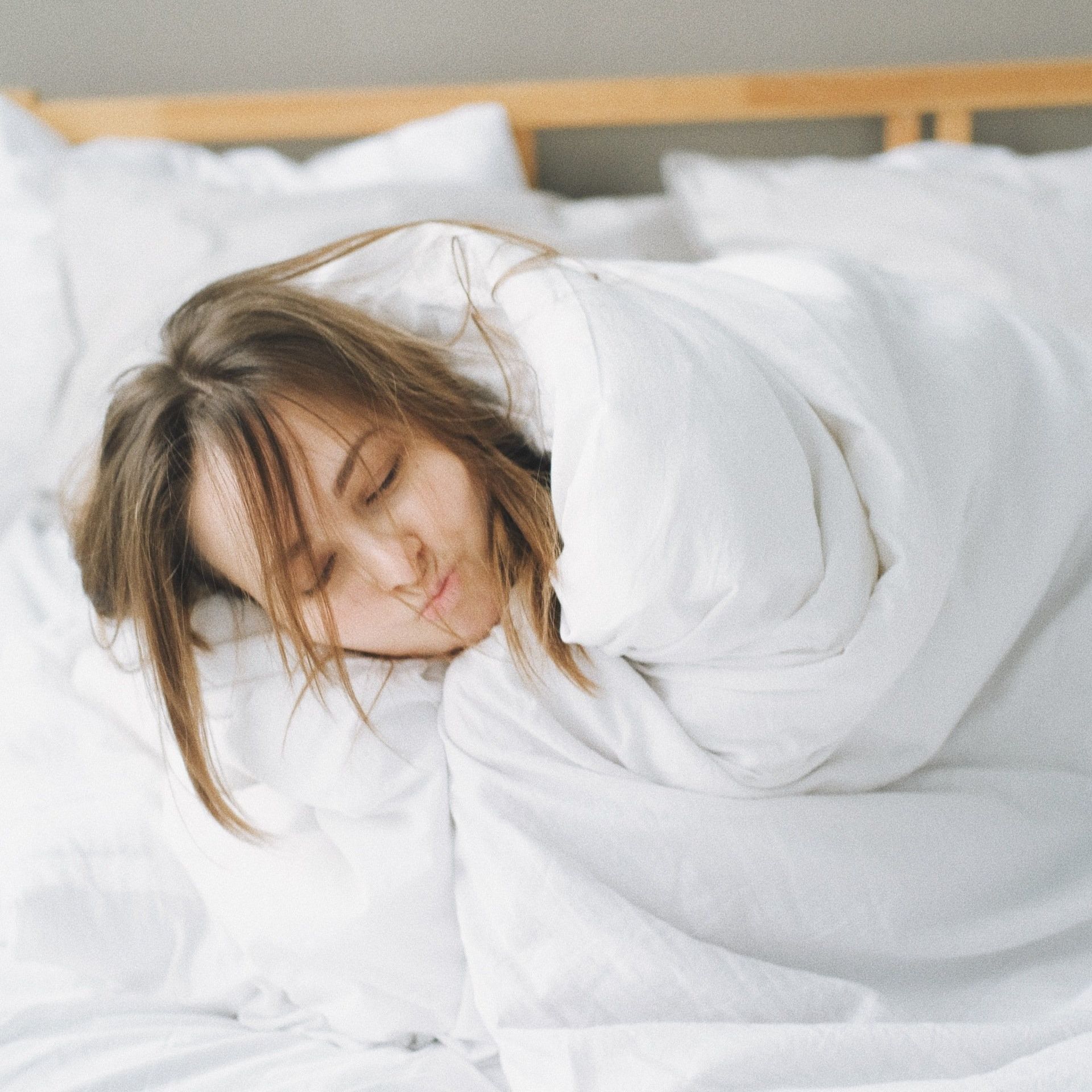 Una donna avvolta in una coperta bianca dorme su un letto