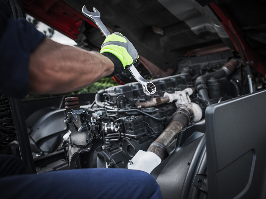 A man is working on a truck engine with a wrench.