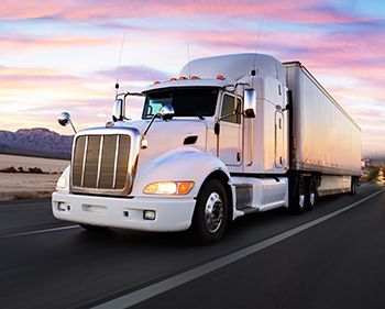 A white semi truck is driving down a highway at sunset.