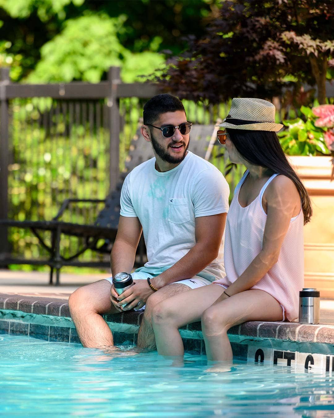 A man and a woman are sitting on the edge of a swimming pool.