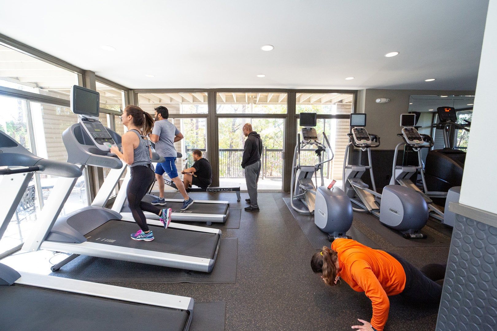 A man is doing push ups in a gym while a woman is running on a treadmill.