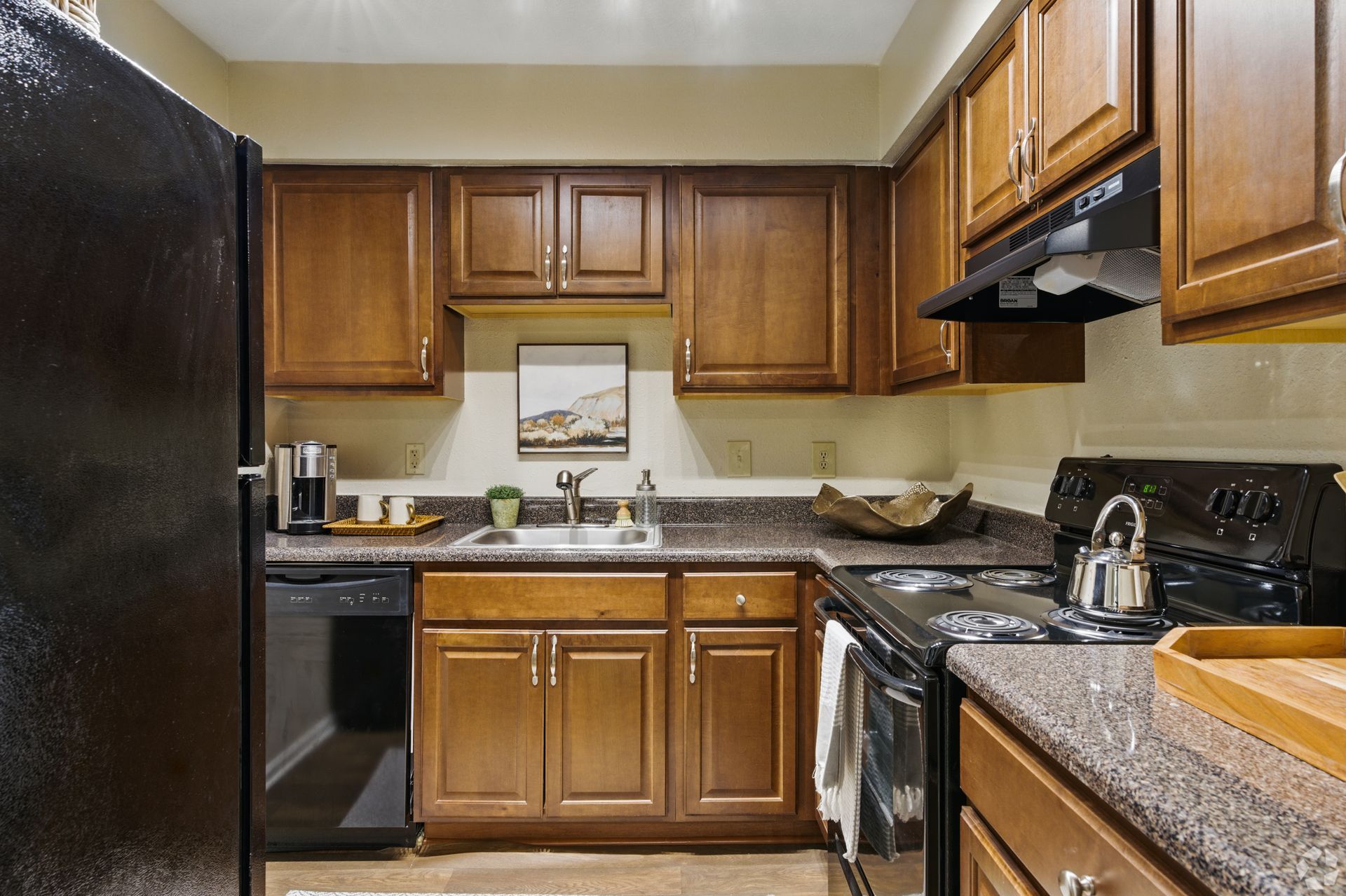 Kitchen with brown cabinets, black appliances, and speckled countertops.