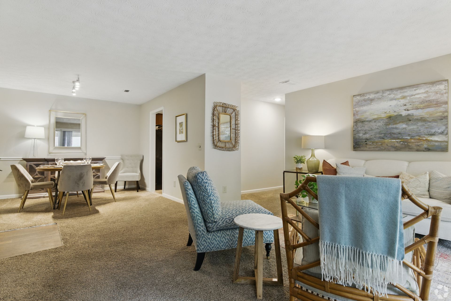 Spacious living room with dining area and neutral tones. Beige carpet, art, and seating create a cozy atmosphere.